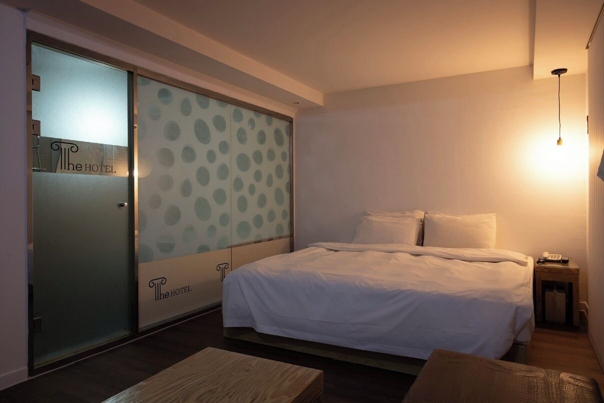 A hotel room with a bed, a nightstand, a wooden bench, and a sliding door with a polka dot pattern.