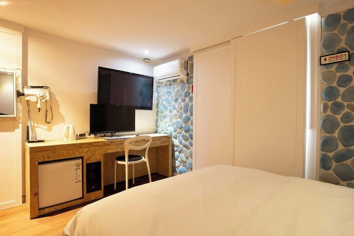 Una camera d'albergo con un letto, una scrivania con un computer, una sedia, una televisione, un telefono e un piccolo frigorifero.