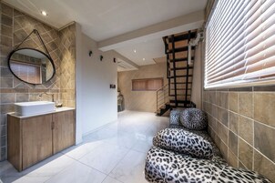 A modern bathroom with a large sink, a mirror, and a leopard-print bench.