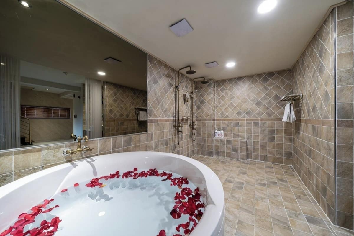 Un bagno moderno con una vasca da bagno freestanding piena di petali di rosa, una doccia a filo pavimento e un grande specchio.