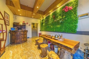 A bar area with a wooden counter, stools, and a green wall with plants. - Lijiang cloud color · July time Inn (Lijiang)