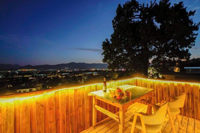 An outdoor seating area with a table and chairs, surrounded by a wooden fence, overlooking a cityscape at dusk.