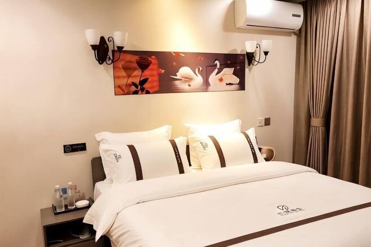 Una habitació d'hotel amb un llit, obra d'art penjada a la paret i una tauleta de nit amb articles de tocador.