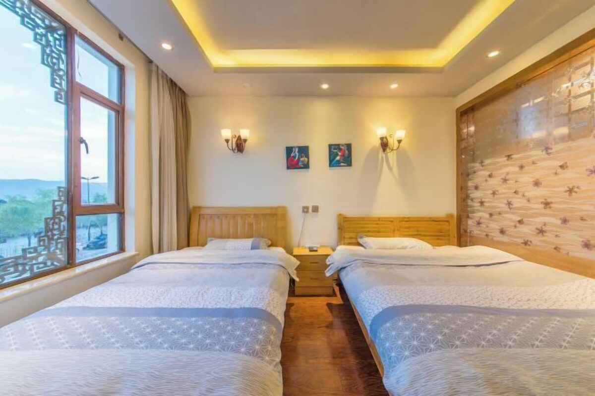 A hotel room with two beds, a window with a view, wall-mounted lights, and a wooden headboard.