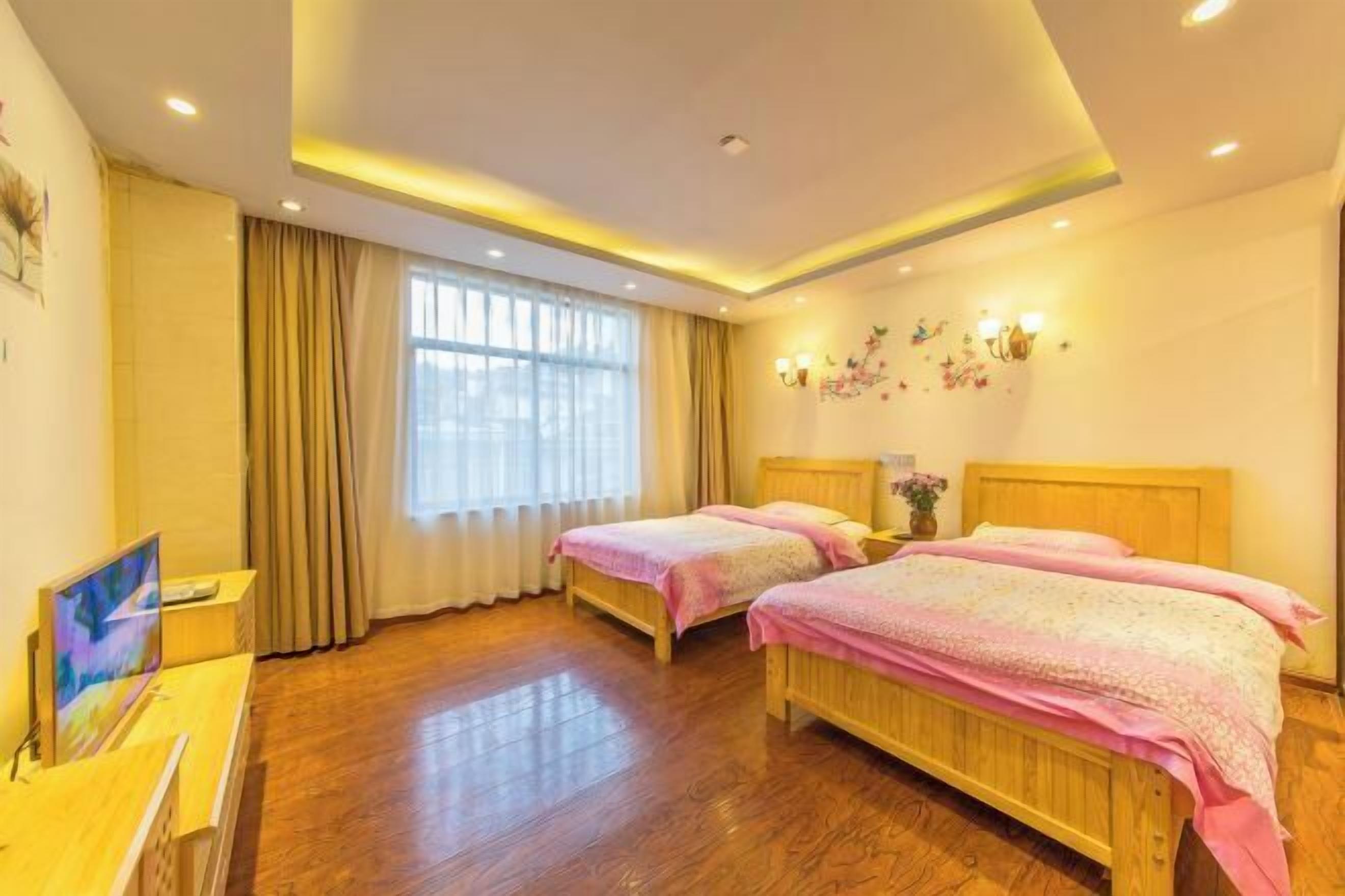 A hotel room with two wooden beds, a TV, a desk, and a large window with curtains.