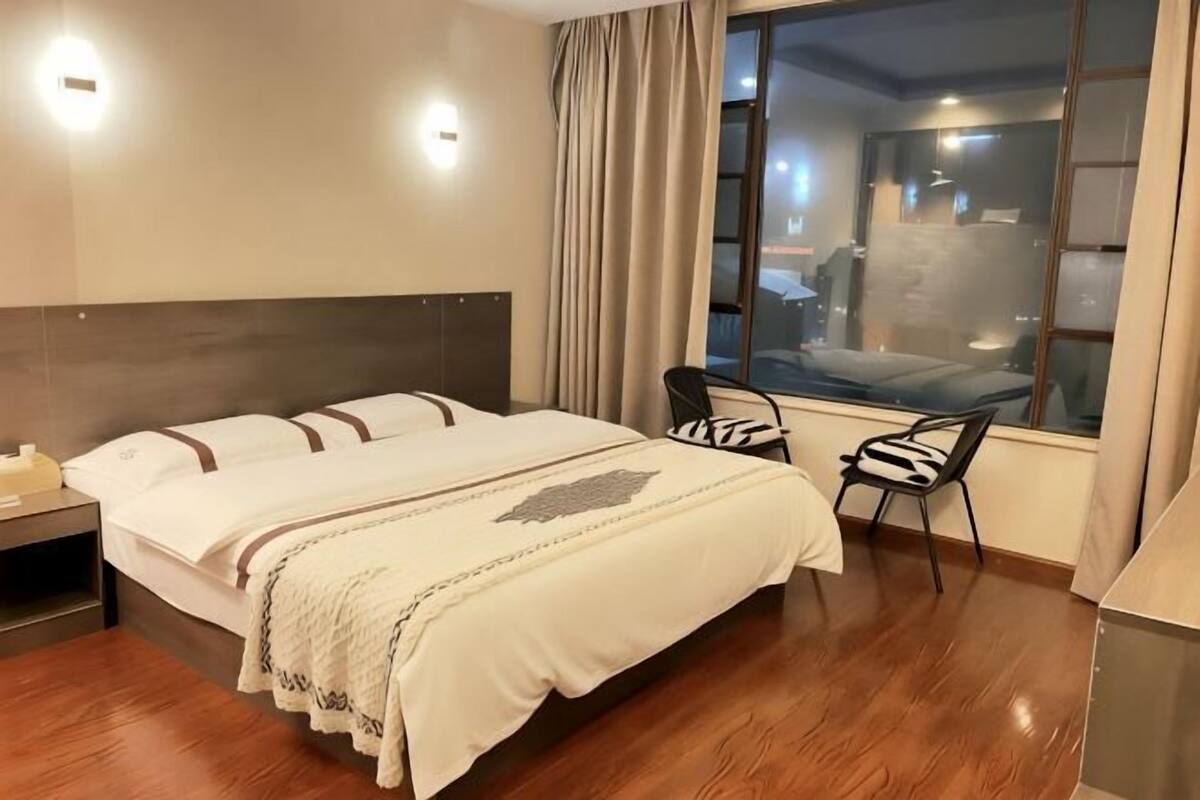 Habitació d'hotel amb un llit, un escriptori, una cadira i una finestra gran.
