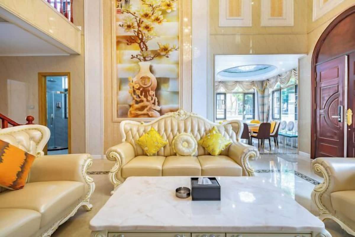 Um lobby luxuoso com uma mesa de centro de mármore, um sofá bege macio com almofadas amarelas e um painel decorativo na parede.