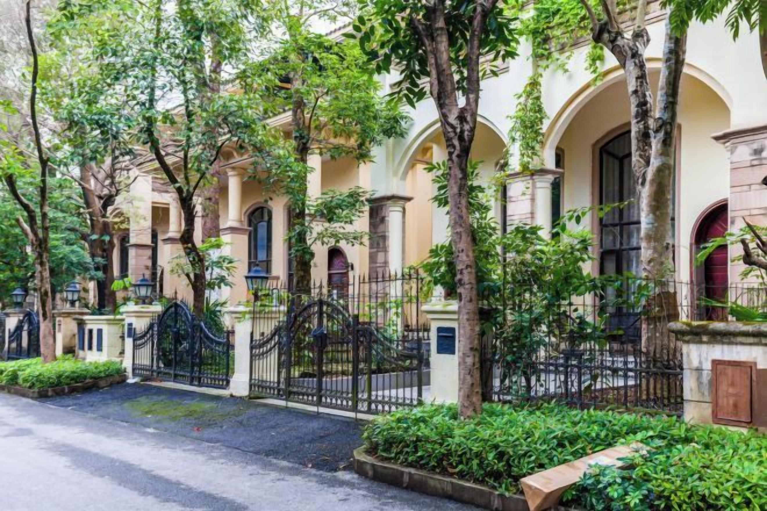 A building with arched windows and a gated entrance, surrounded by trees and greenery.