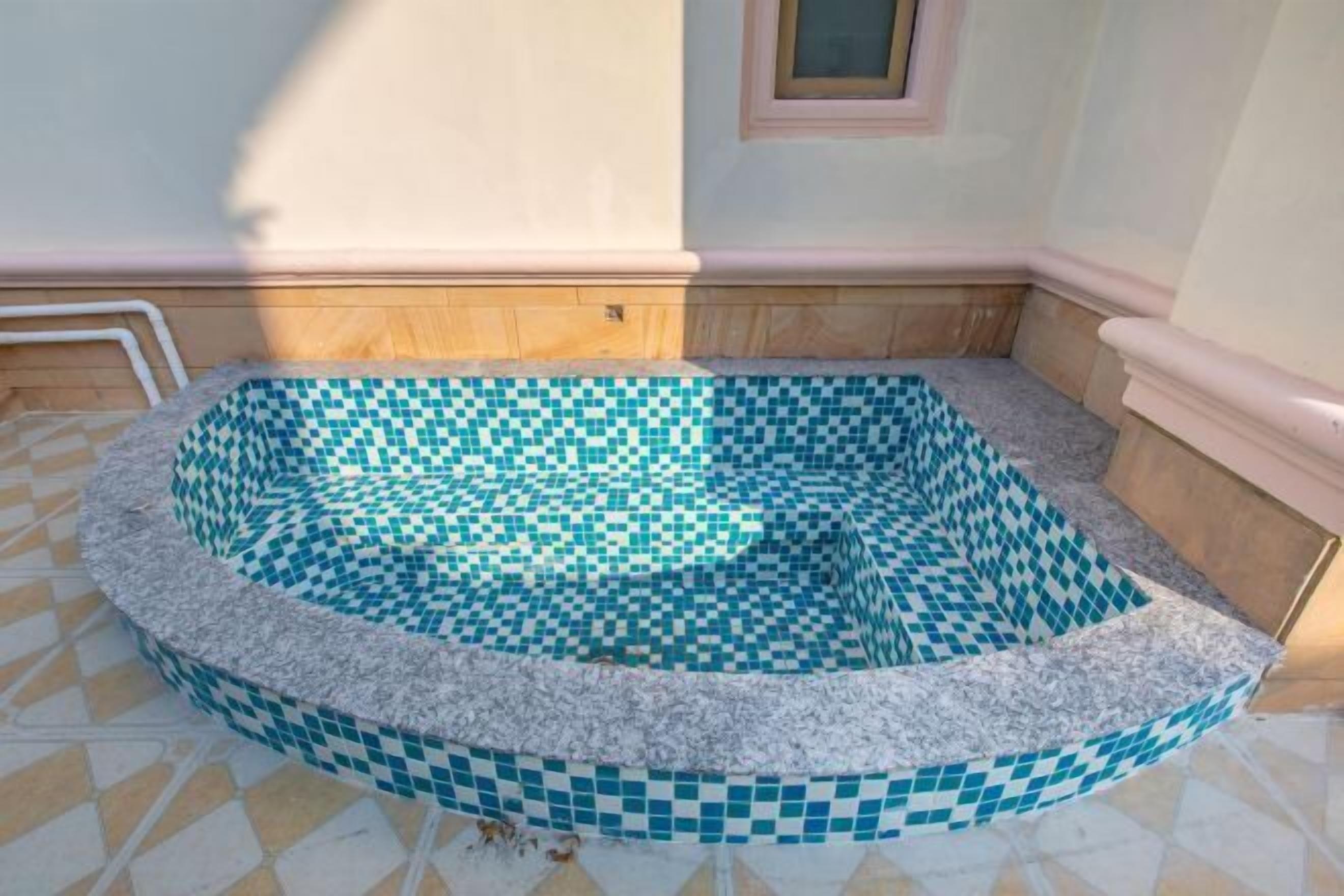 Un jacuzzi rond, orné d’un motif de carreaux en damier, entouré d’une bordure en pierre, installé sur un sol carrelé et adossé à un mur de couleur claire.
