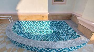 Un jacuzzi rond, orné d’un motif de carreaux en damier, entouré d’une bordure en pierre, installé sur un sol carrelé et adossé à un mur de couleur claire.