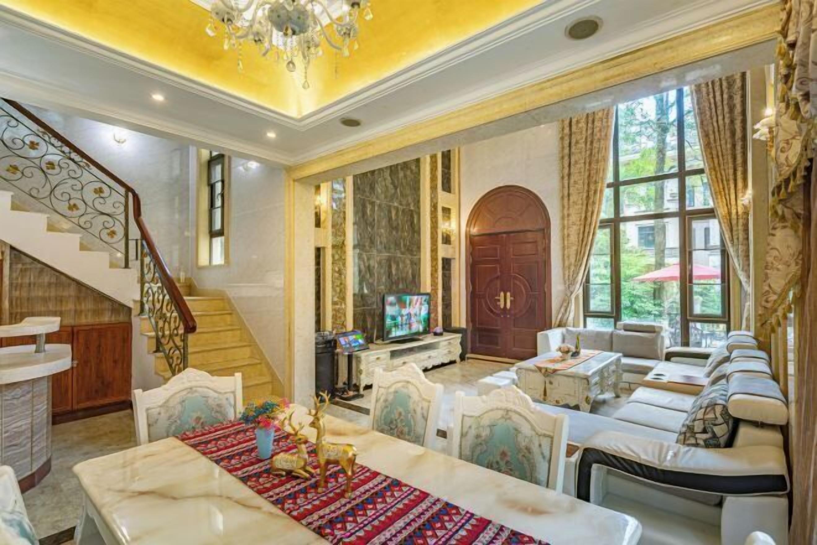 Un vaste salon agrémenté d’un escalier en marbre, d’une grande porte en arc de cercle et d’un coin salon confortable avec un canapé et des fauteuils.