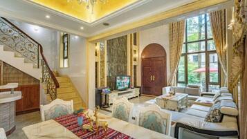 Un vaste salon agrémenté d’un escalier en marbre, d’une grande porte en arc de cercle et d’un coin salon confortable avec un canapé et des fauteuils.