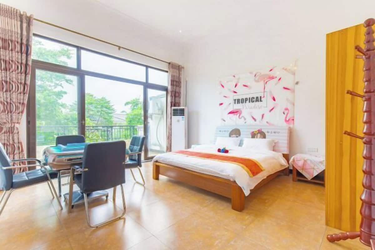 Quarto com cama, escrivaninha, cadeiras, janela com cortinas e um pôster com tema tropical.