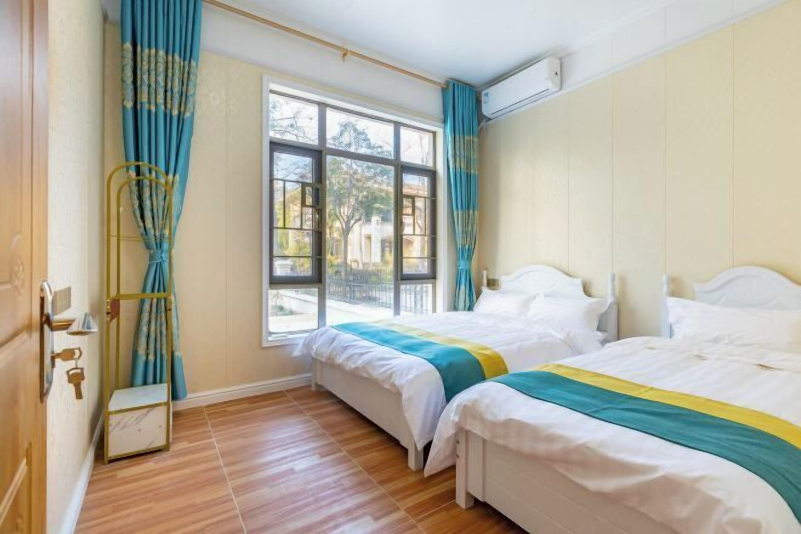 A room with two beds, a window, curtains, and a wooden floor.
