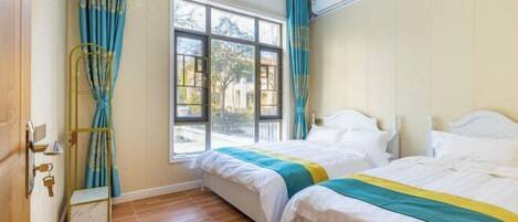 A room with two beds, a window, curtains, and a wooden floor.