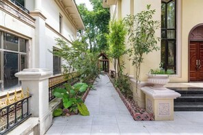 A narrow, paved pathway flanked by lush greenery and architectural features, including a decorative railing and a stone planter. - Qingyuan Hengda Yilin Yashe Drifting Holiday Villa (Qingyuan)