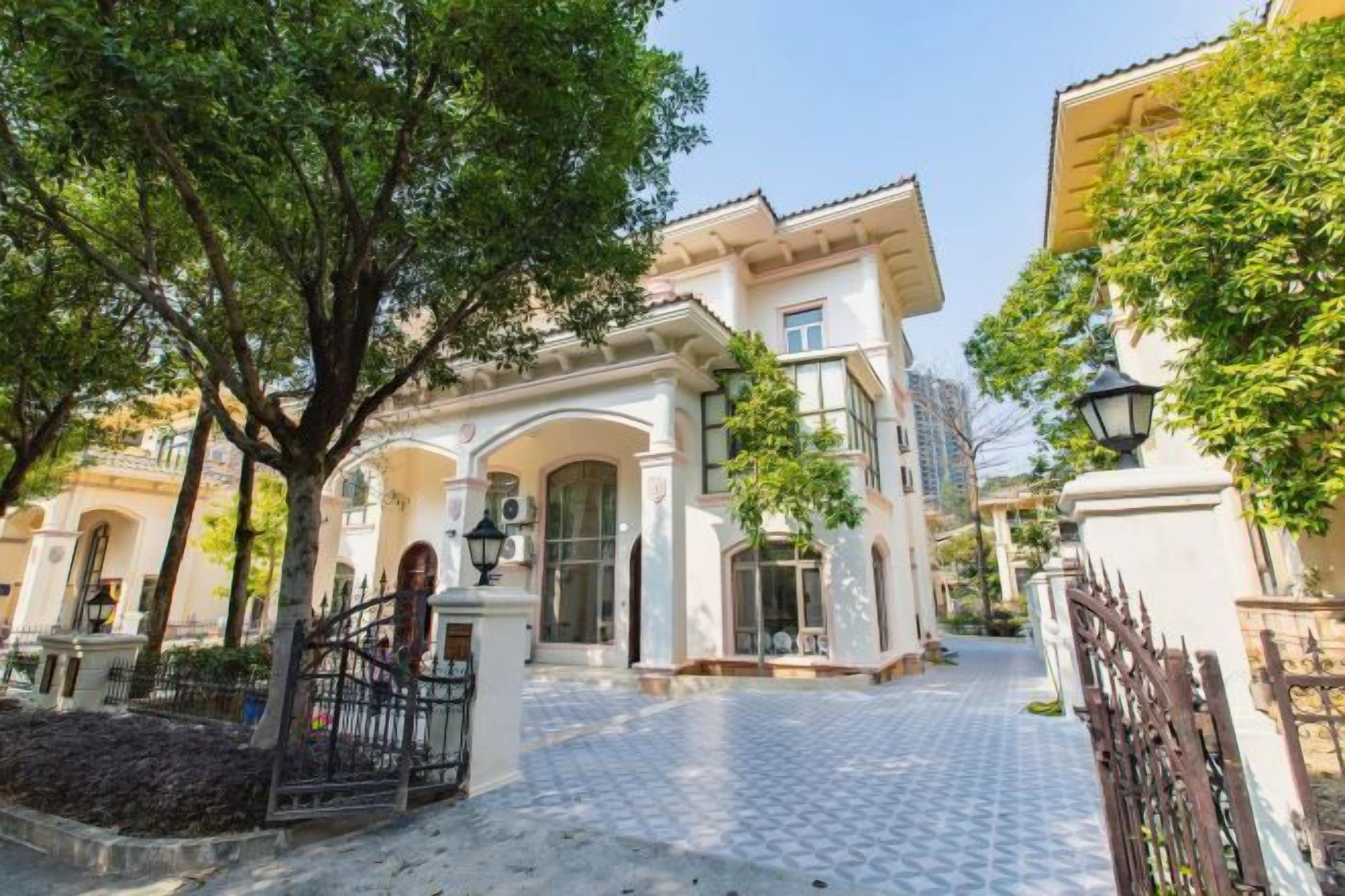 A courtyard with a paved walkway, a gated entrance, and a building with arched windows and a tiled roof.