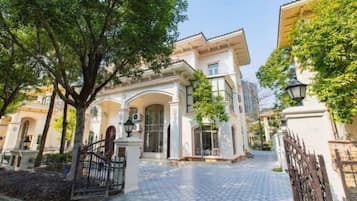 A courtyard with a paved walkway, a gated entrance, and a building with arched windows and a tiled roof.