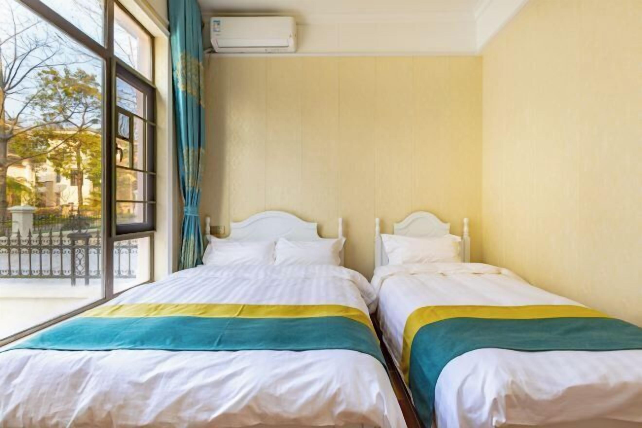 A hotel room with two beds, a window with a view of the outside, and an air conditioning unit on the wall.
