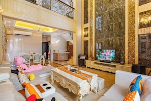 A spacious living room with a high ceiling, a television, plush seating, and a decorative fireplace. - Qingyuan Hengda Yilin Yashe Drifting Holiday Villa (Qingyuan)
