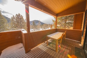 A wooden deck with a table and chairs, overlooking a snowy mountain landscape.