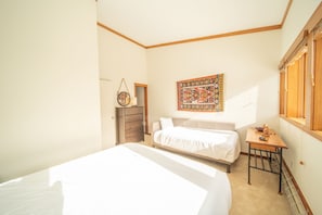 A bedroom with a large bed, a dresser, a small table, and a wall-mounted tapestry.