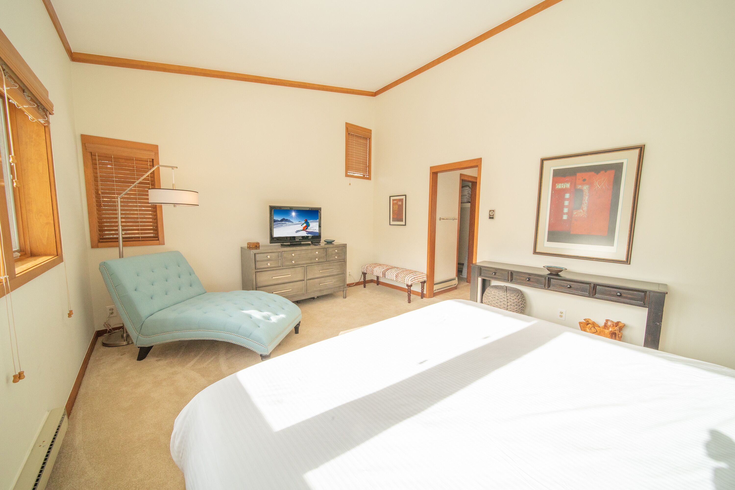 A bedroom with a large bed, a dresser, a chair, a television, and a framed picture on the wall.