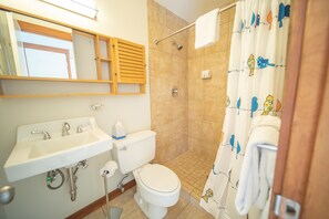 A bathroom with a sink, toilet, shower, and a mirror with a wooden frame.