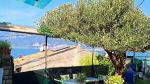 An outdoor patio with a table and chairs, surrounded by greenery and a view of the sea. - Gaspar House (Brenzone sul Garda)