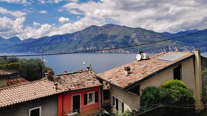 A coastal building with a red facade, a tiled roof, and a view of the sea and mountains in the background. - Gaspar House (Brenzone sul Garda)