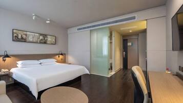 Een moderne hotelkamer met een groot bed, nachtkastjes, een ronde tafel, een stoel, een televisie en een schuifdeur naar een badkamer.