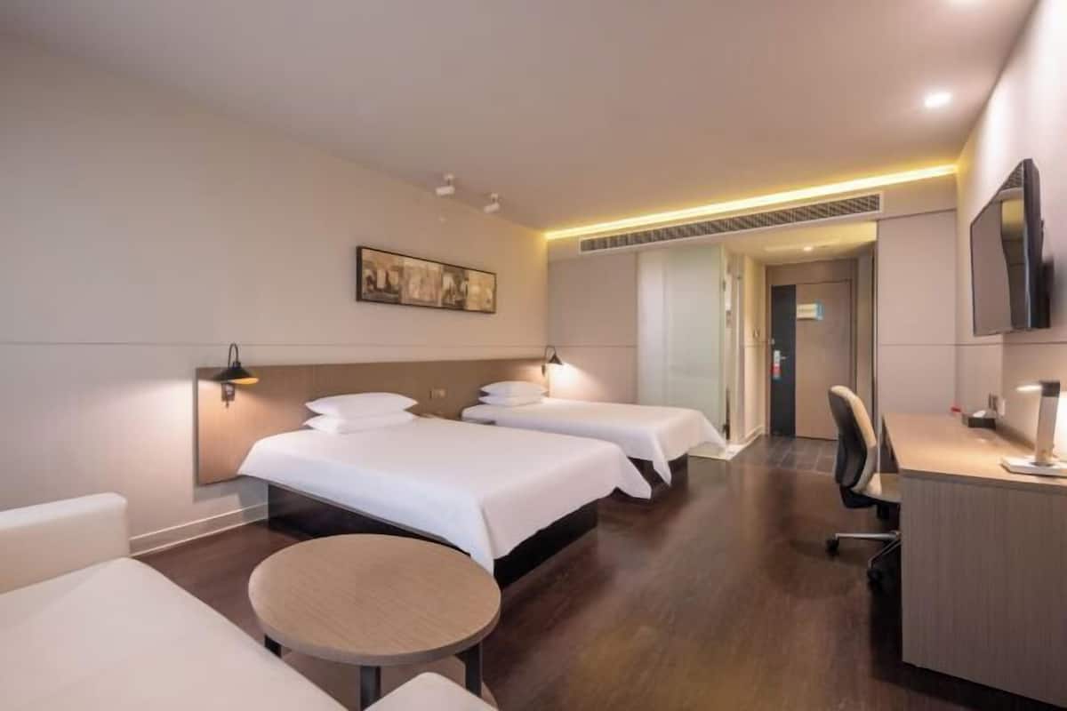 Quarto de hotel com duas camas, uma escrivaninha, uma cadeira, uma mesa redonda e um quadro na parede.