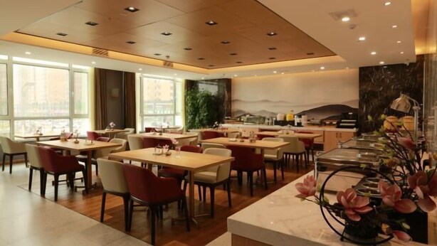 Een modern restaurant met meerdere eettafels en stoelen, een marmeren toonbank en een groot raam met uitzicht op de stad.