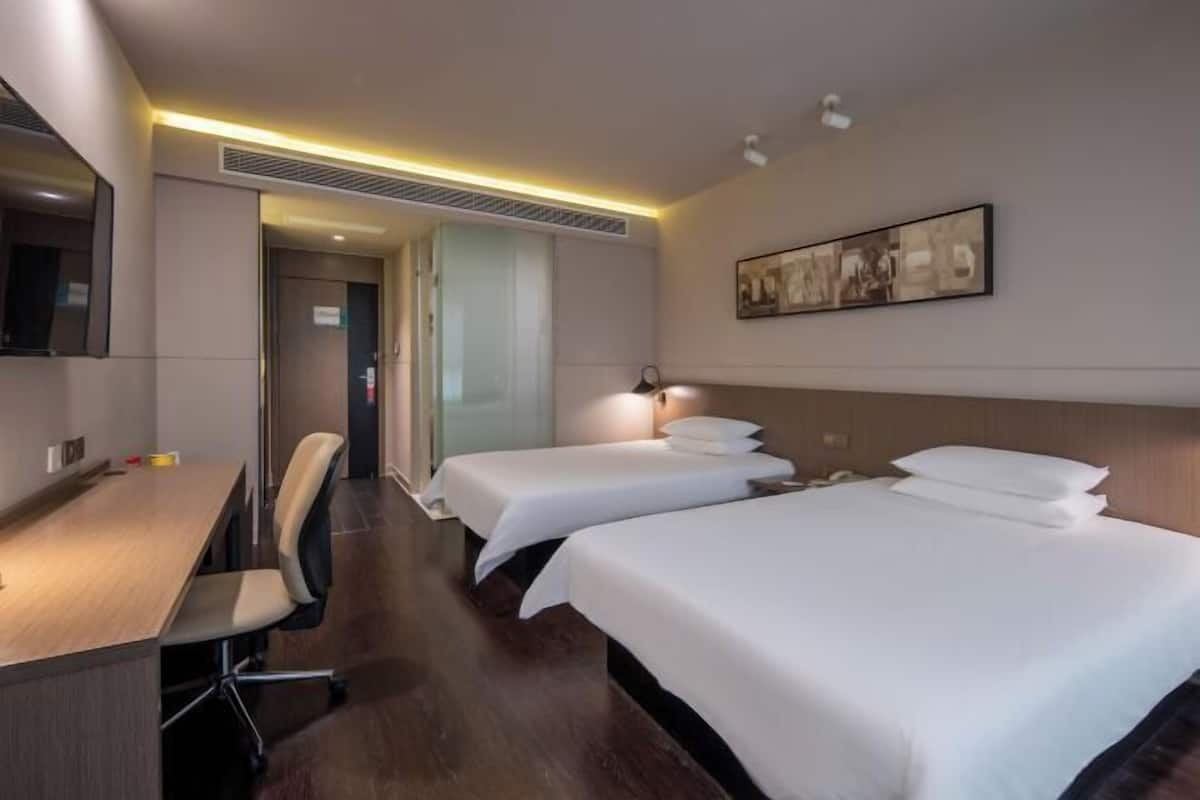 Quarto de hotel com duas camas, uma escrivaninha e uma cadeira.