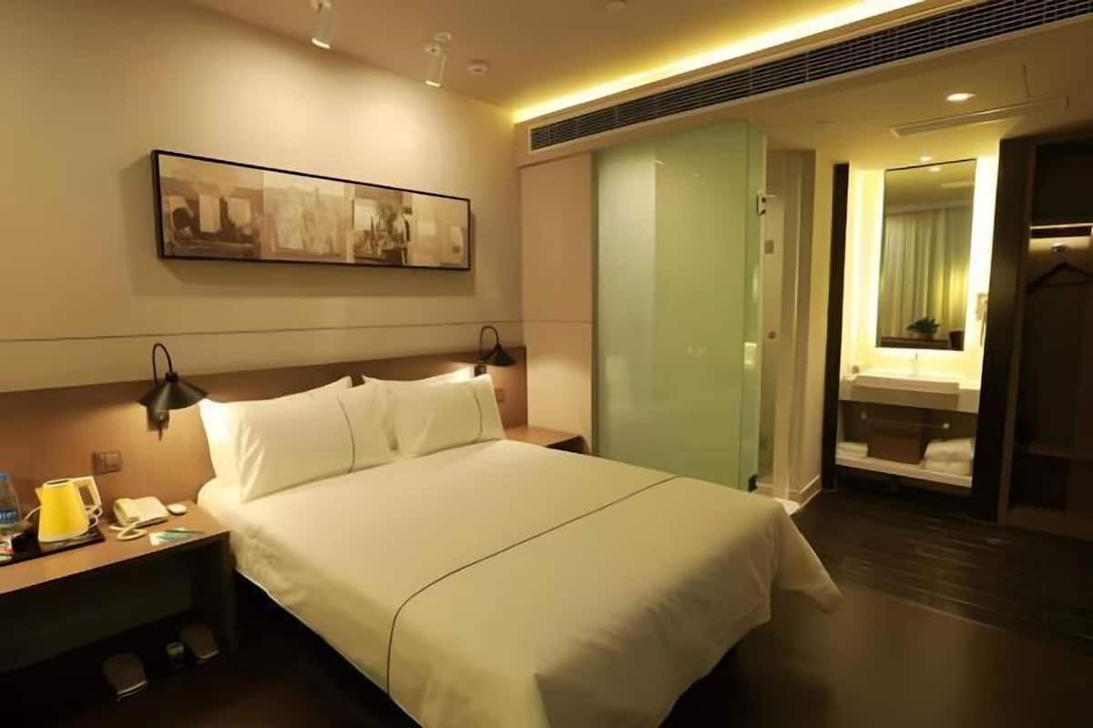 Quarto de hotel com cama, mesa de cabeceira, luminária, telefone e um quadro na parede.