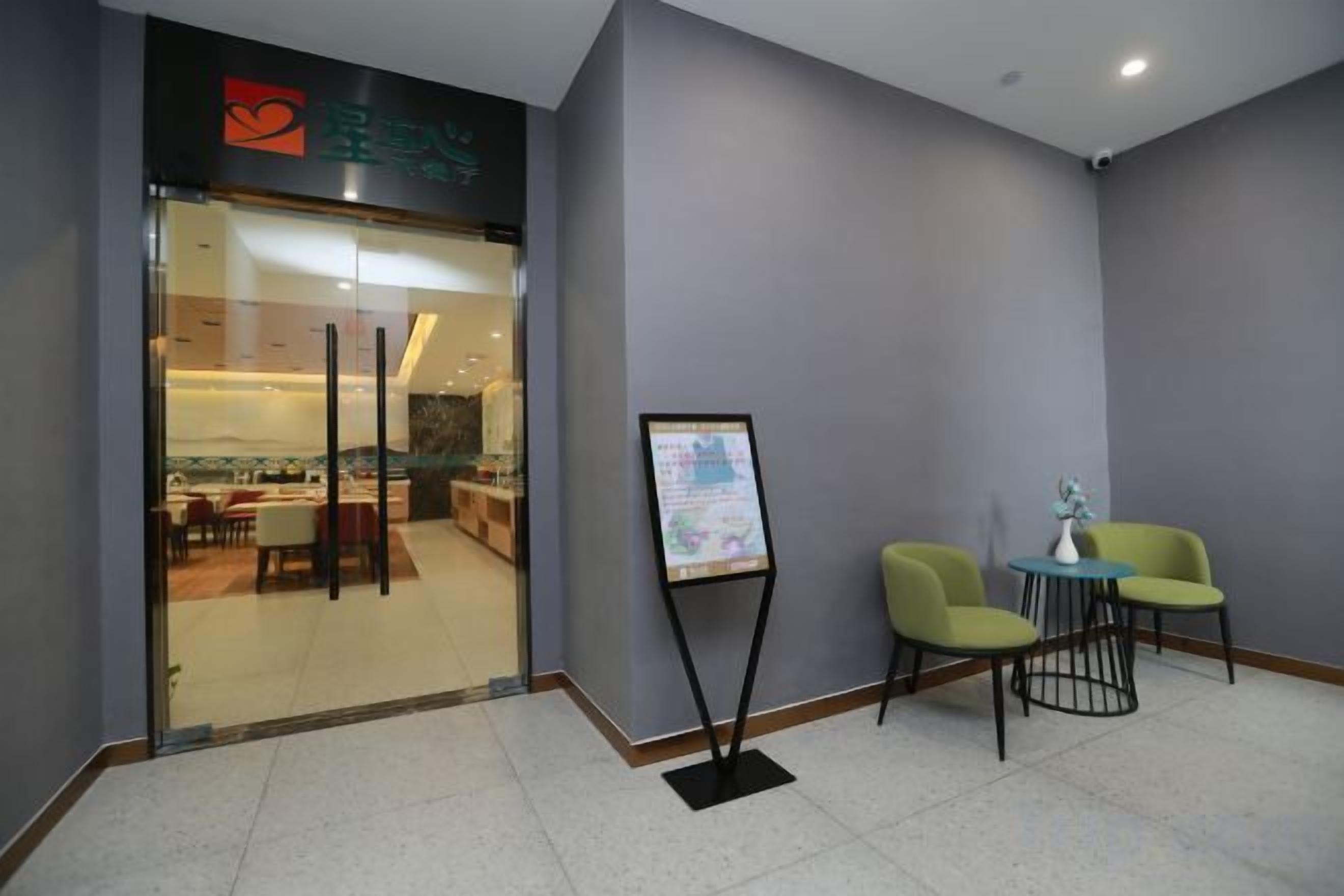 A hotel reception area with a glass door entrance, a reception desk, and two green chairs.