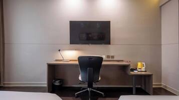 Hotelkamer met een bed, een bureau met stoel, een aan de muur bevestigde televisie en een tafeltje met lamp.