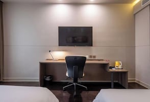 Habitación de hotel con cama, escritorio con silla, televisor montado en la pared y una mesita de noche con lámpara.