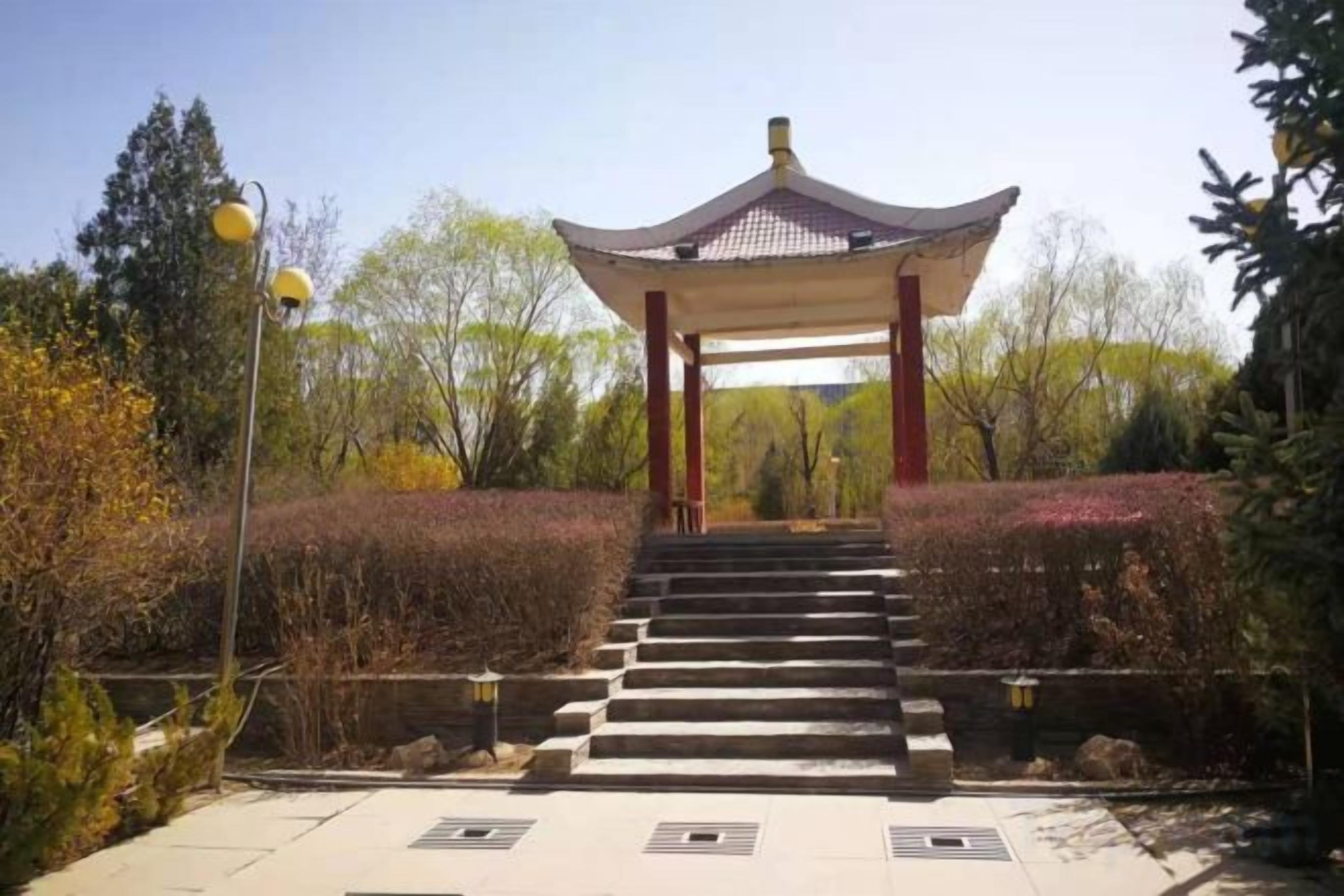 A traditional pavilion with a tiled roof, surrounded by a landscaped garden with steps leading up to it.