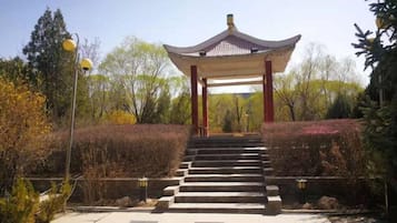 A traditional pavilion with a tiled roof, surrounded by a landscaped garden with steps leading up to it.
