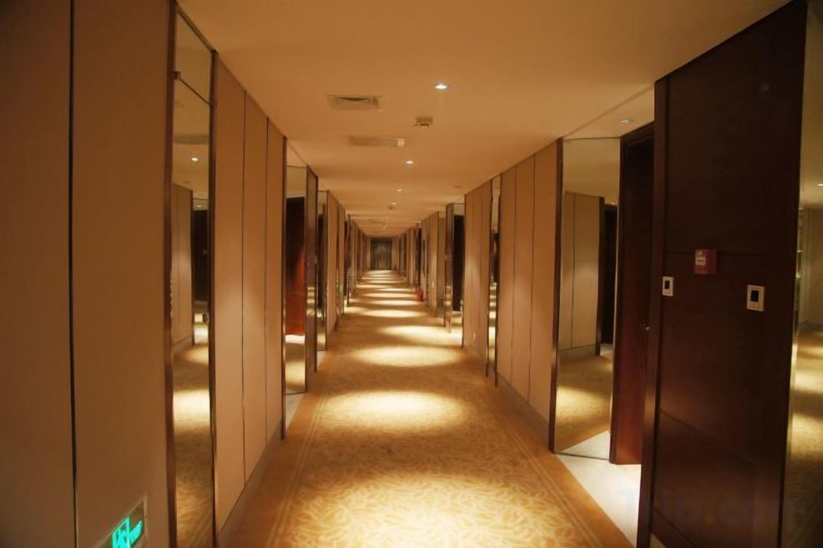 Un long couloir étroit aux murs recouverts de miroirs et dont les portes sont disposées d’un seul côté, menant à une pièce.