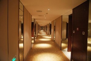 Un pasillo largo y estrecho con paredes espejadas y puertas a un lado, que conduce a una habitación.