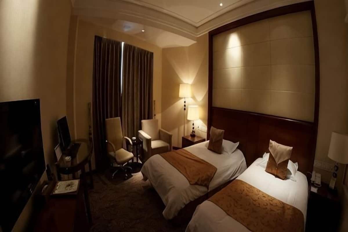 A hotel room with two beds, a desk, a chair, a TV, and a large window with curtains.