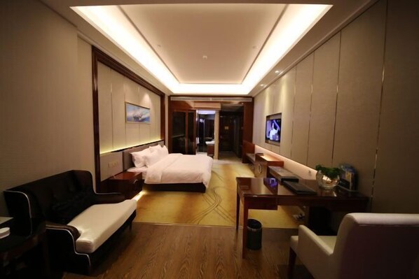 A hotel room with a bed, a sofa, a desk, a TV, and a small table with a plant. - Jinchang Hotel (Jinchang)