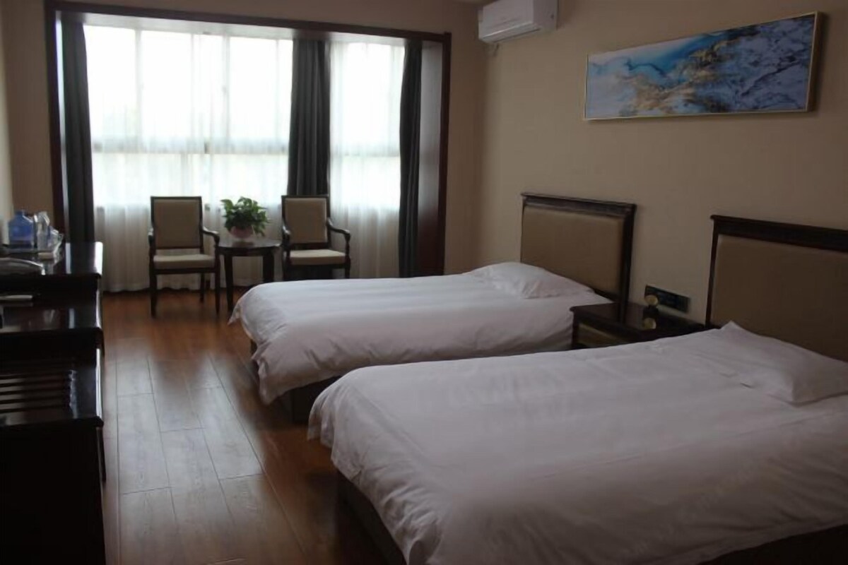A hotel room with two beds, a desk with a chair, a potted plant, and a painting on the wall.