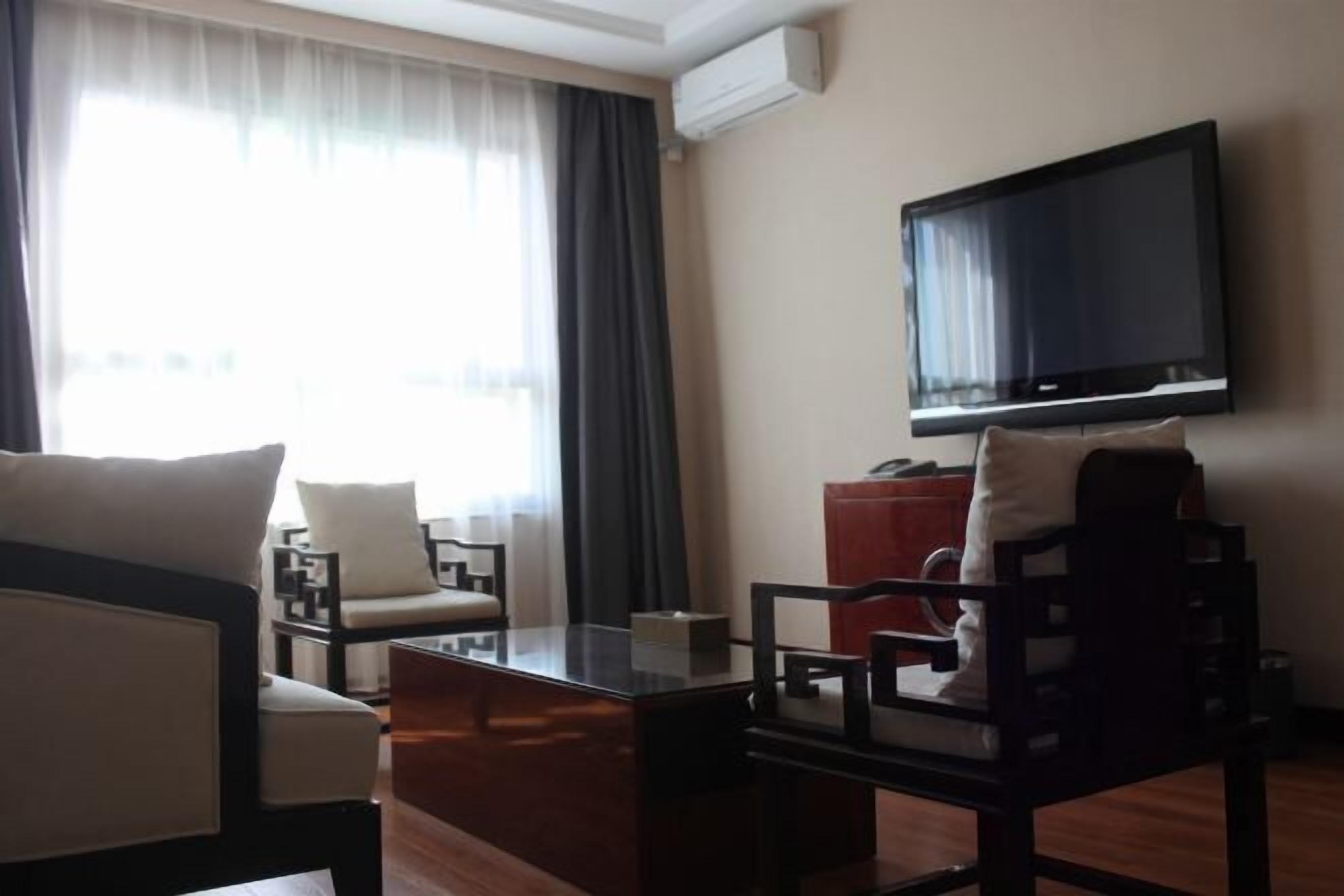 Habitació d'hotel amb televisió de pantalla plana penjada a la paret, taula de cafè de fusta, dues butaques, un sofà i una finestra gran amb cortines.