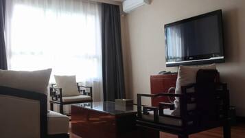 Habitació d'hotel amb televisió de pantalla plana penjada a la paret, taula de cafè de fusta, dues butaques, un sofà i una finestra gran amb cortines.