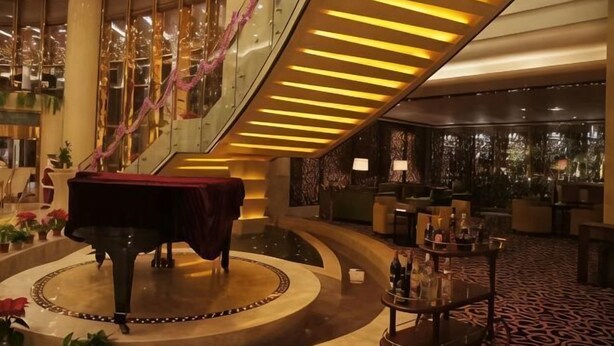 Een statig lobbymiddelstuk met een piano, een trap en een receptiehoek.