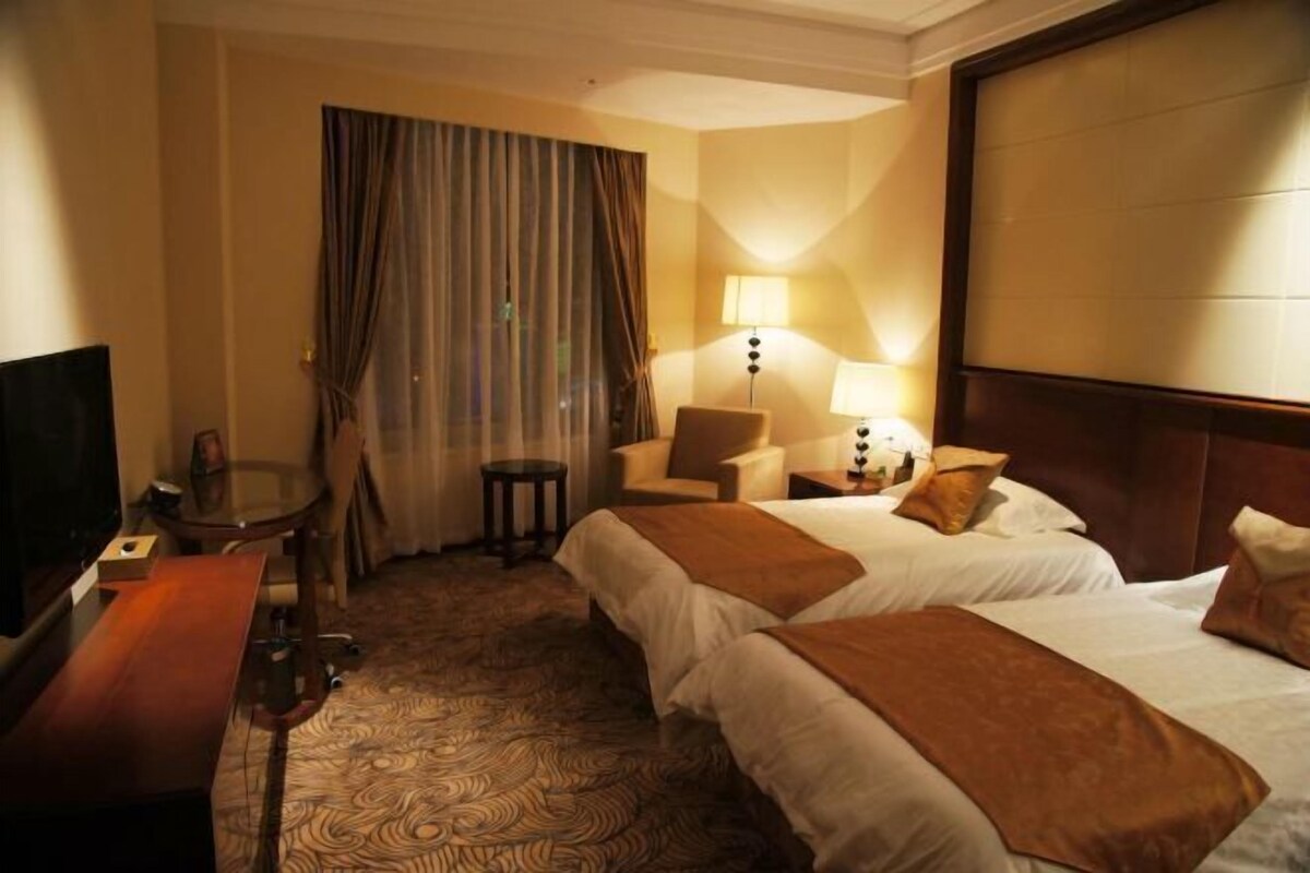 A hotel room with two beds, a television, a desk, and a chair.