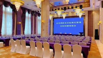 A conference room with rows of white chairs, a stage with a presentation screen, and a chandelier.